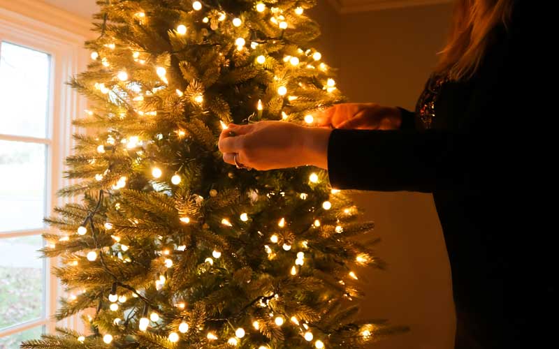 Donna che avvolge una catena di luci intorno all’albero di Natale con posa a spirale